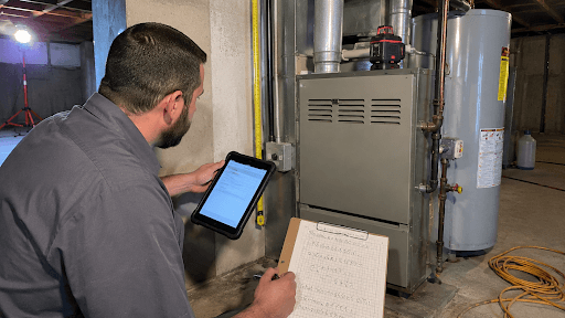 HVAC technician measuring a basement furnace and running a load calculation to determine what size HVAC unit you need for an Indiana home.