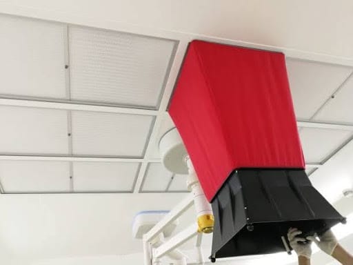 Technician using an airflow capture hood to measure air from a ceiling vent during commercial HVAC air balancing.